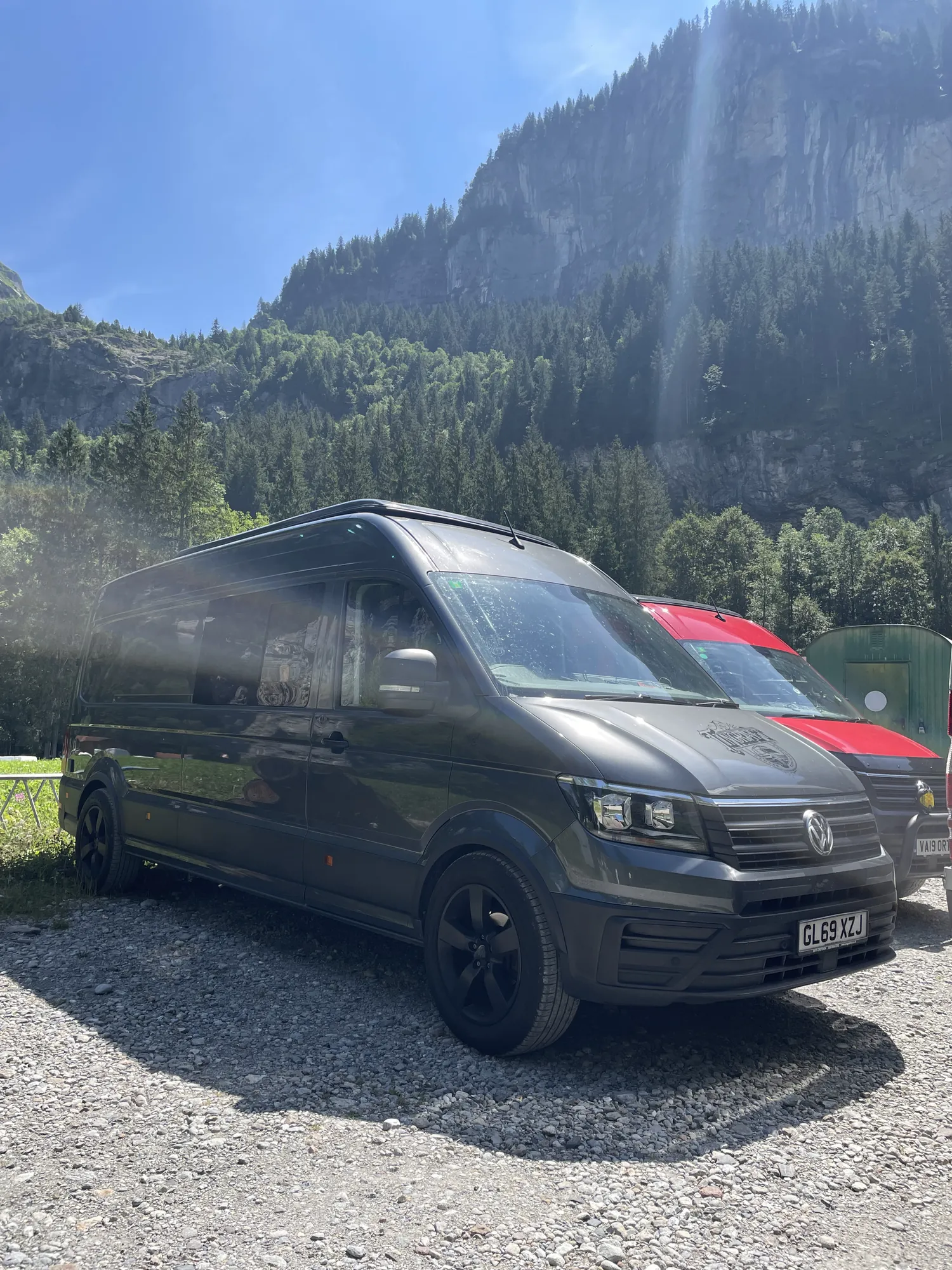 Grey VW Crafter camper parked below alpine cliffs on a touring trip