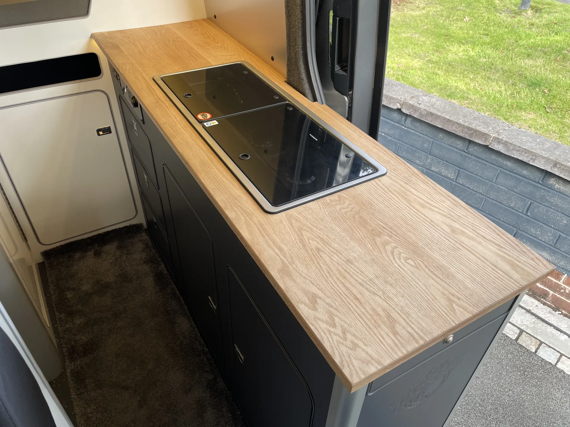 Hob and worktop with the side door open onto greenery in a VW Crafter camper