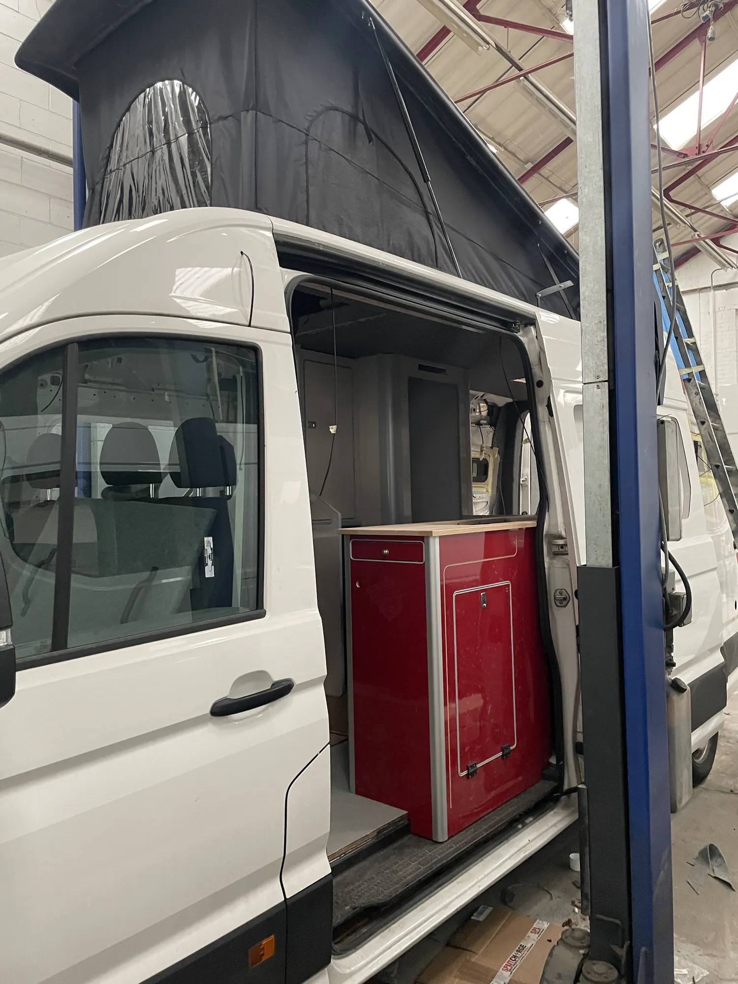 White VW Crafter camper with the side door open and pop-top roof visible