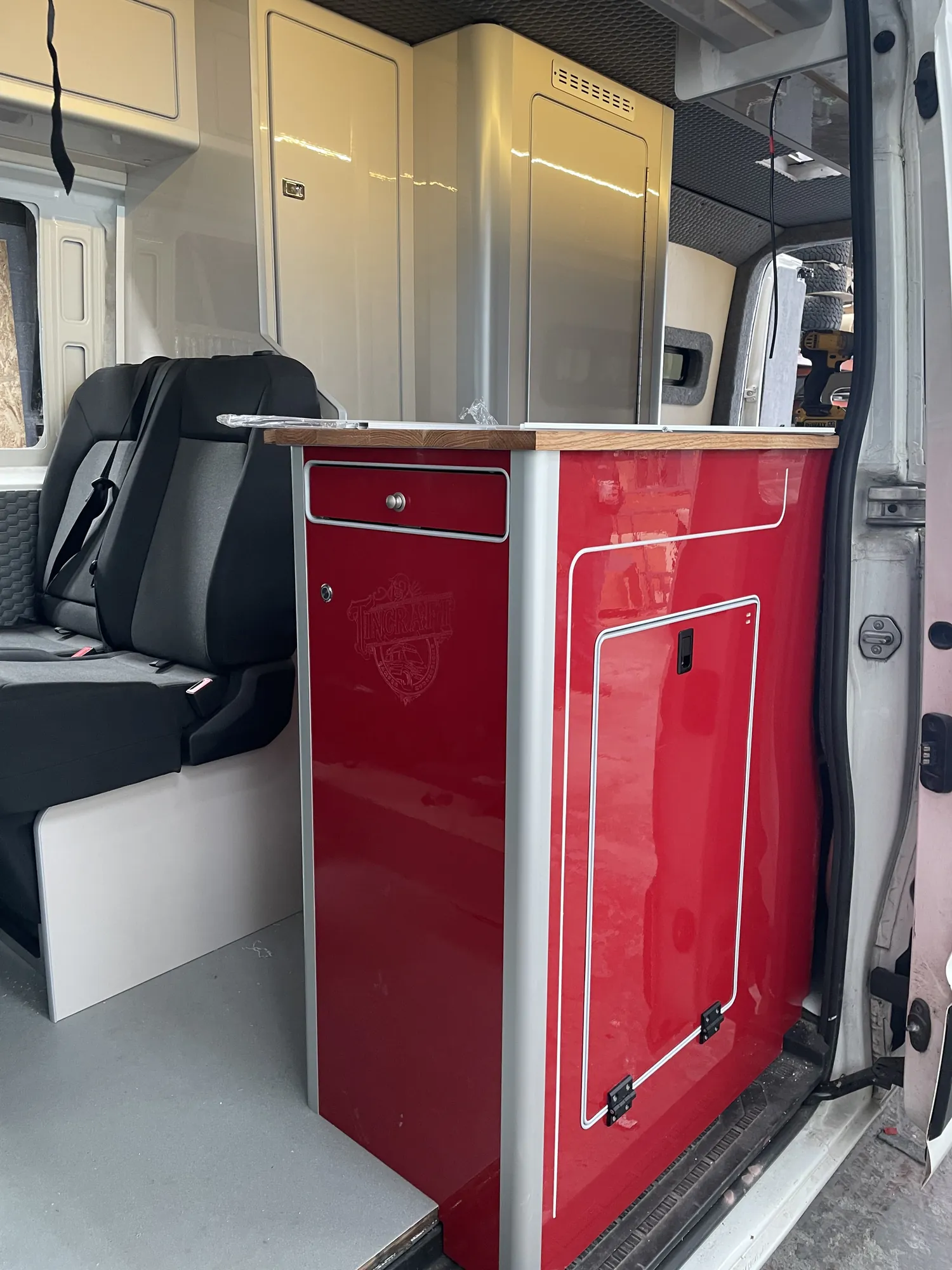Red gloss cabinet beside a seat in a VW Crafter camper conversion