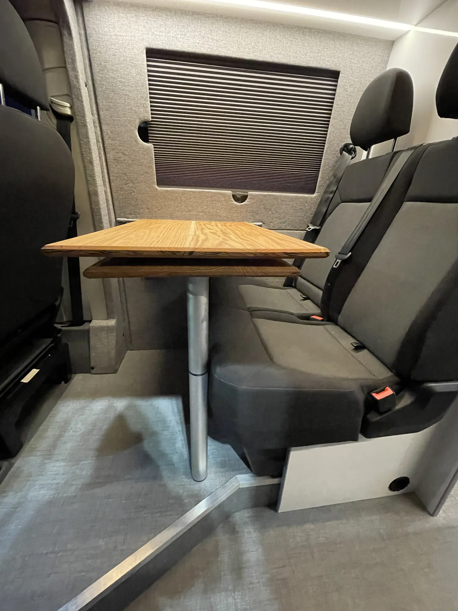 Dining table beside a window with the blind half drawn in a VW Crafter camper