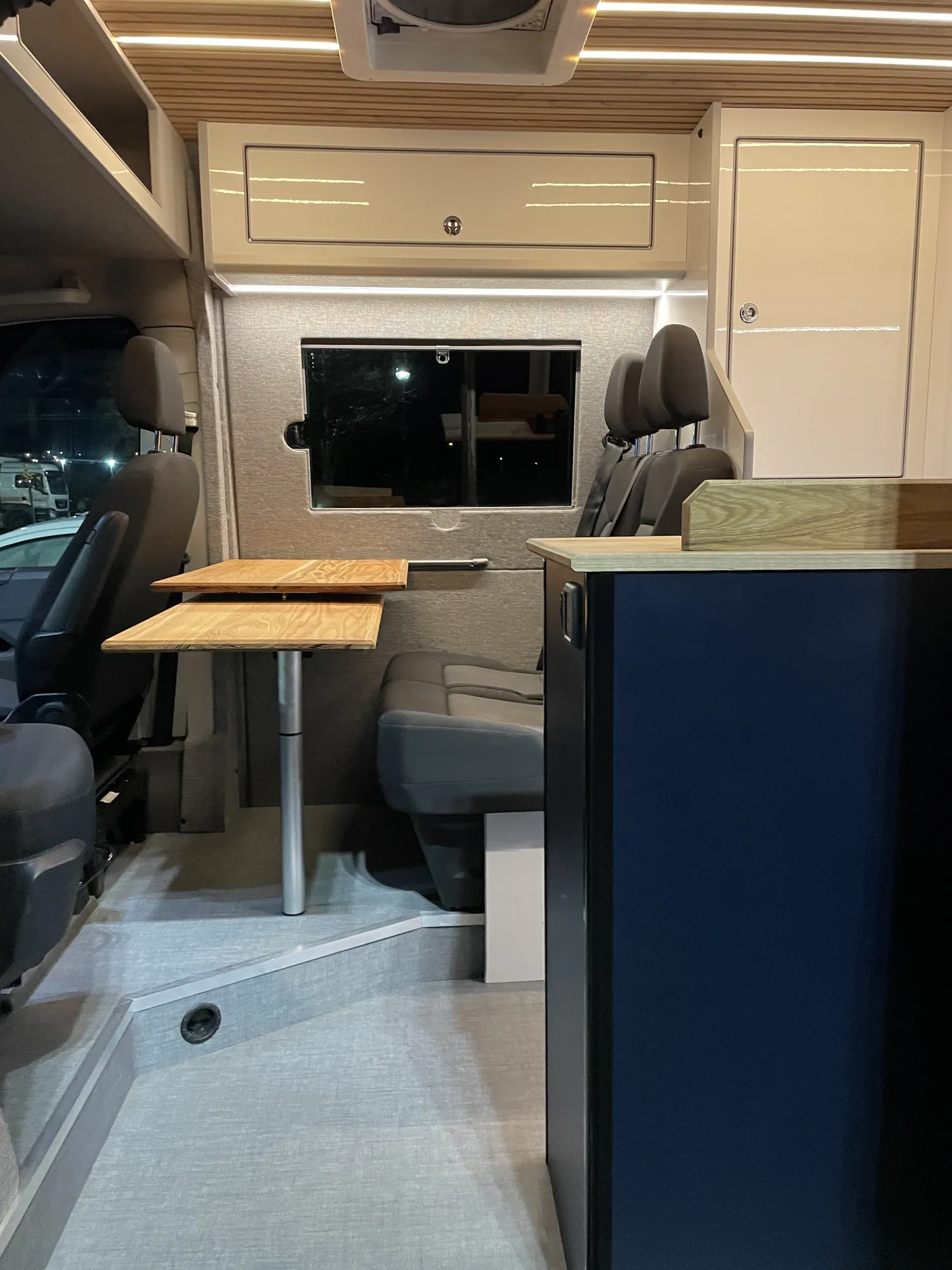 Dinette with navy cabinets and an oak table in a VW Crafter conversion
