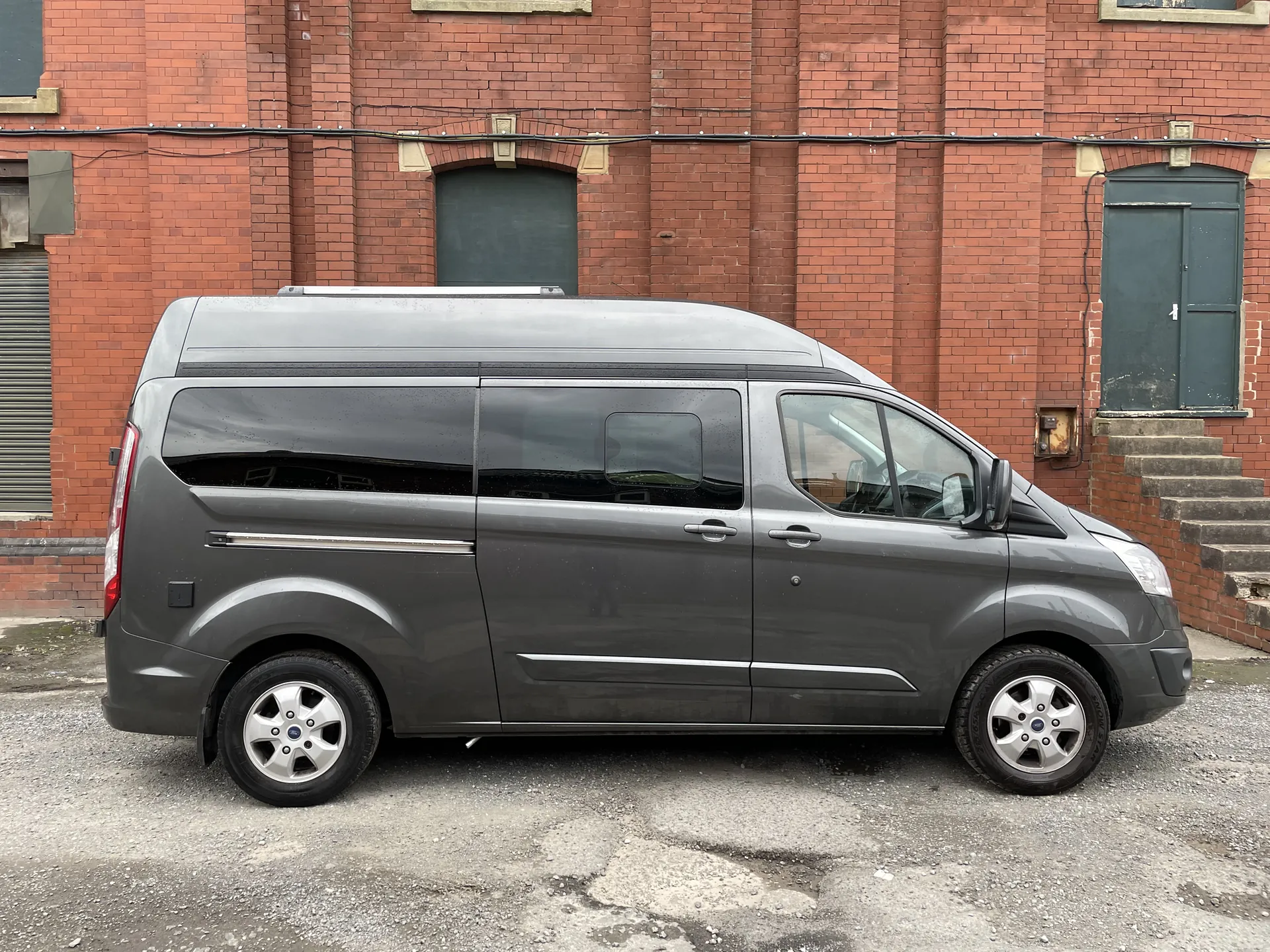 Side profile of a graphite Ford Transit Custom camper against a brick wall