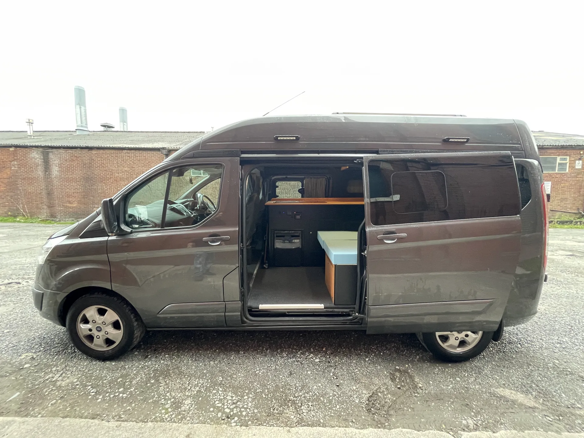 Open side door of a Ford Transit Custom camper showing the galley inside