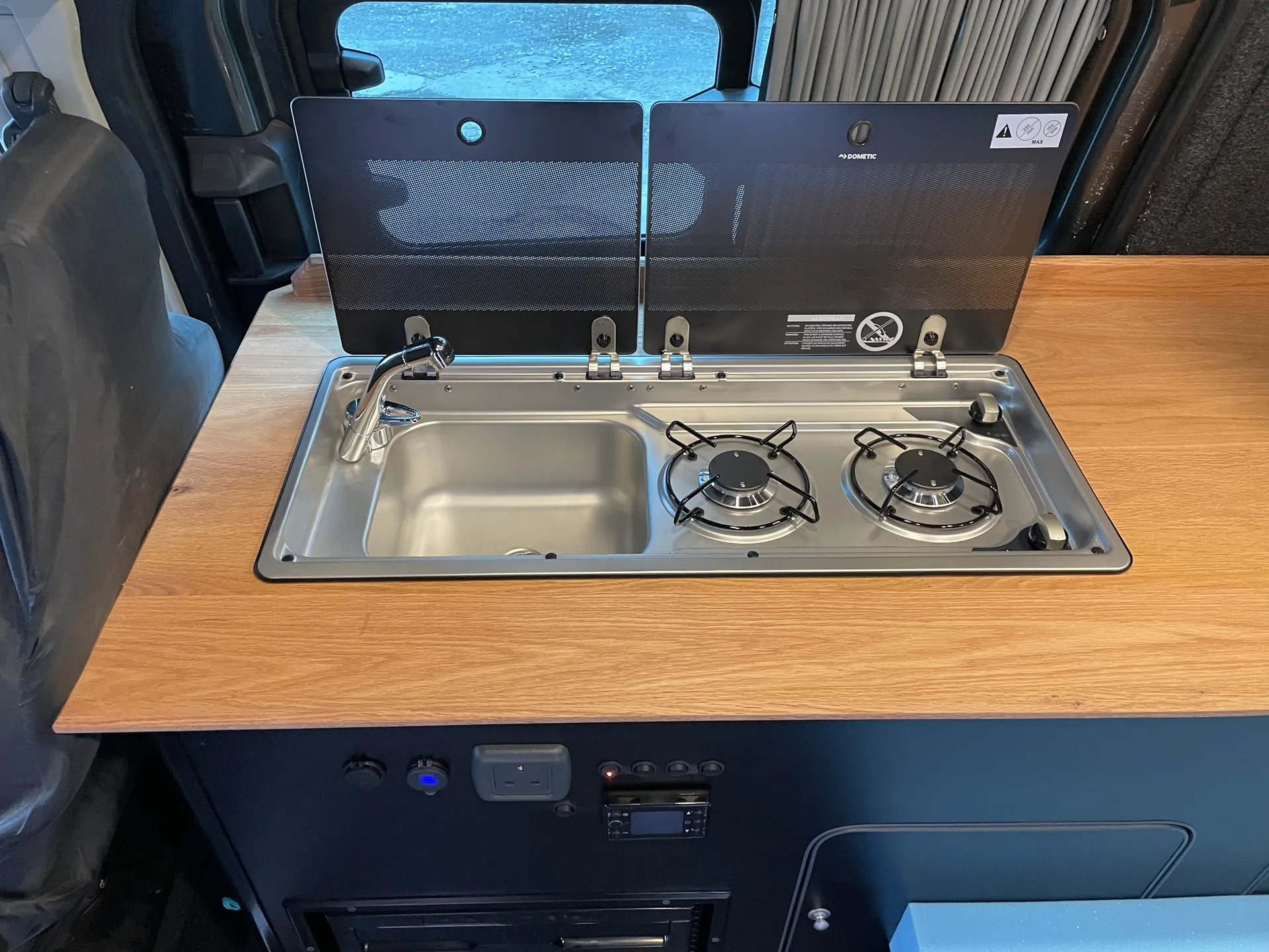 Sink and hob set into a warm-toned worktop in a Ford Transit Custom camper