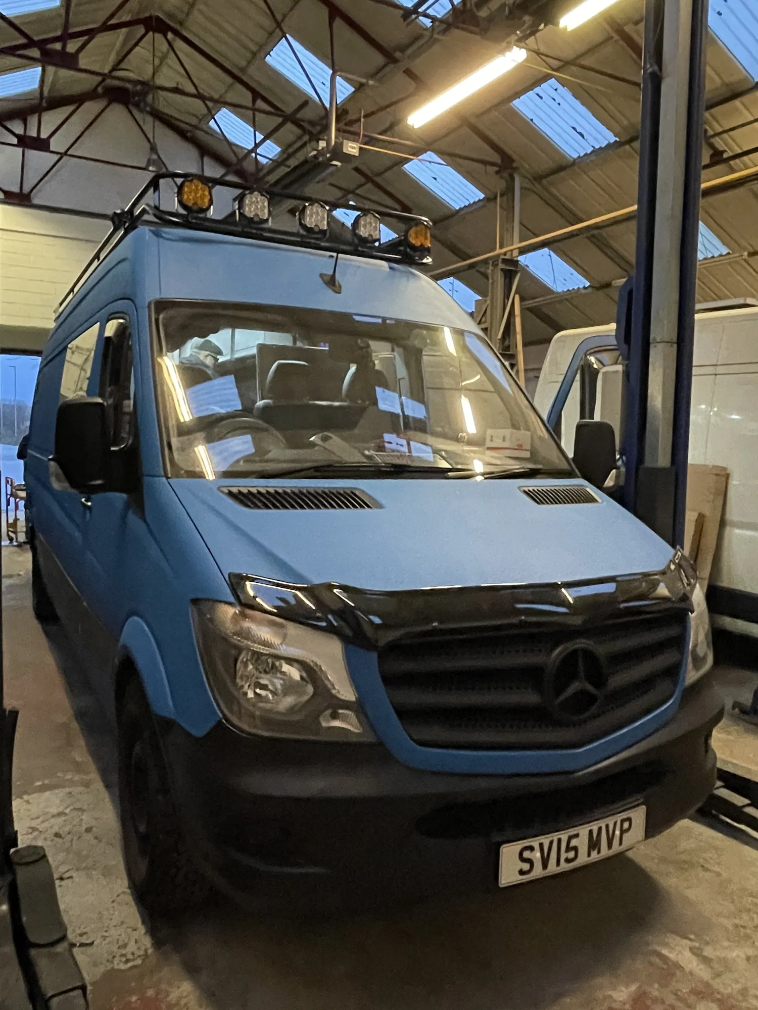 Light blue Mercedes Sprinter expedition camper, front three-quarter view with roof rack