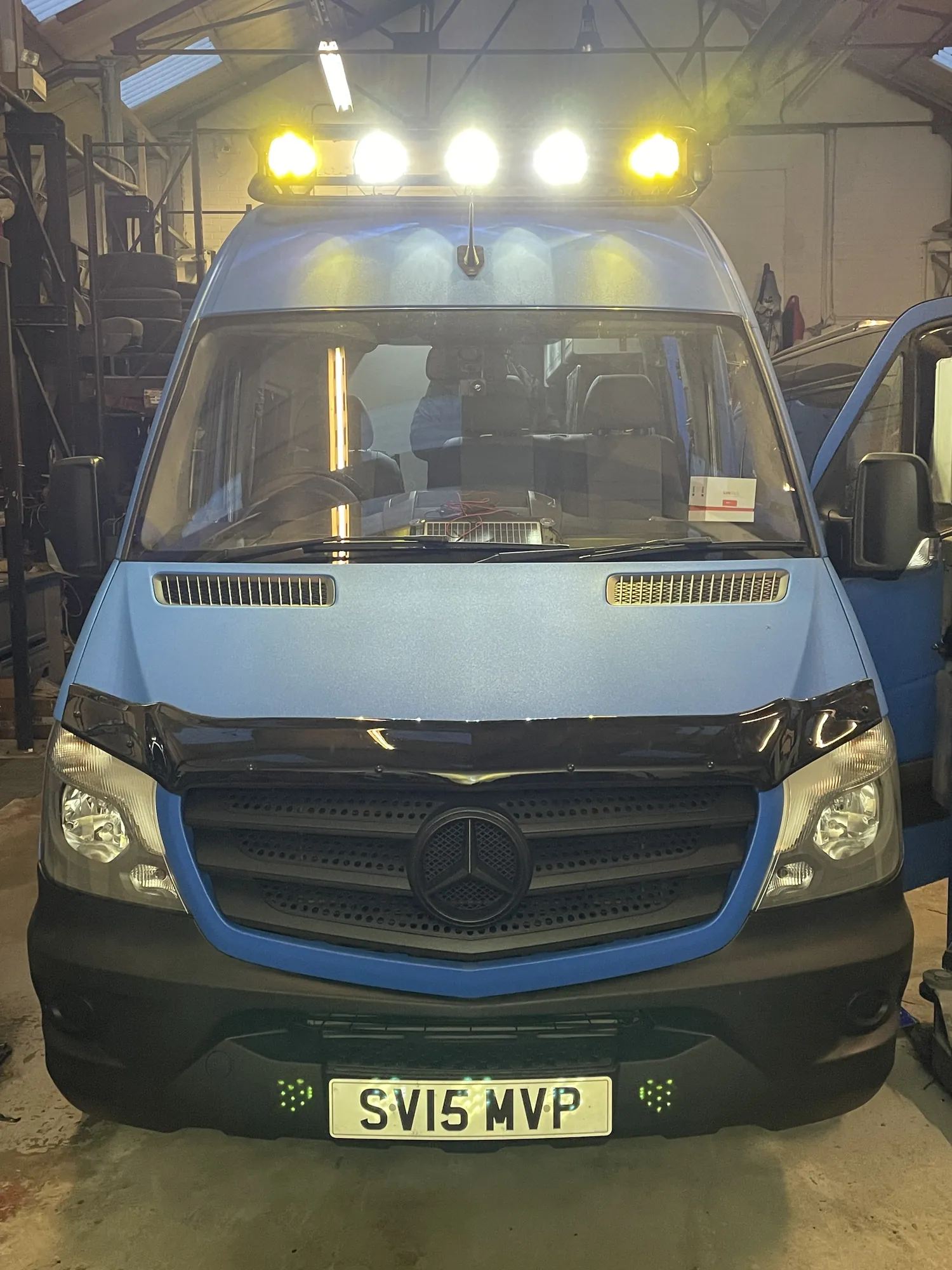 Front view of a blue Sprinter camper with the roof LED light bar lit