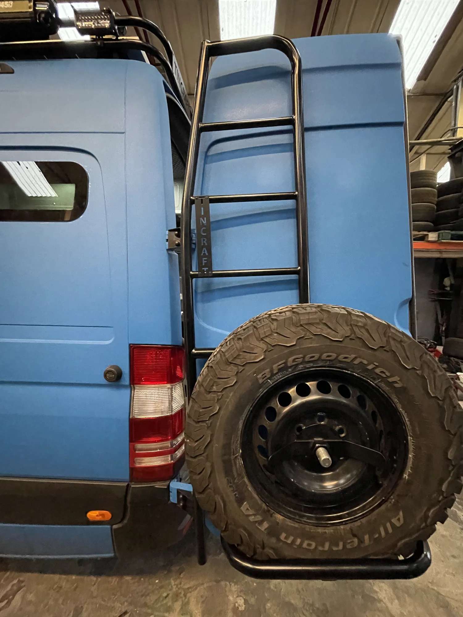 Rear three-quarter view of a blue Sprinter camper with rear spare wheel