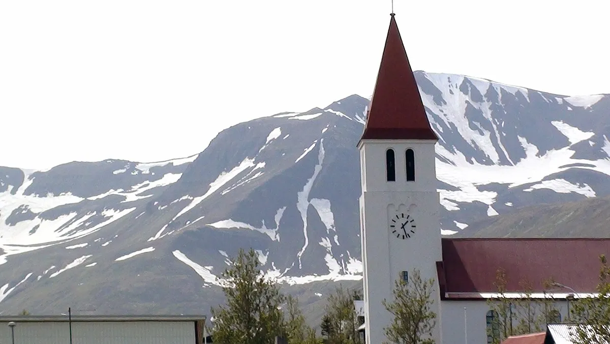 A photo of the church bell tower in Siglufjörður, with typical Icelandic landscape in the background.
