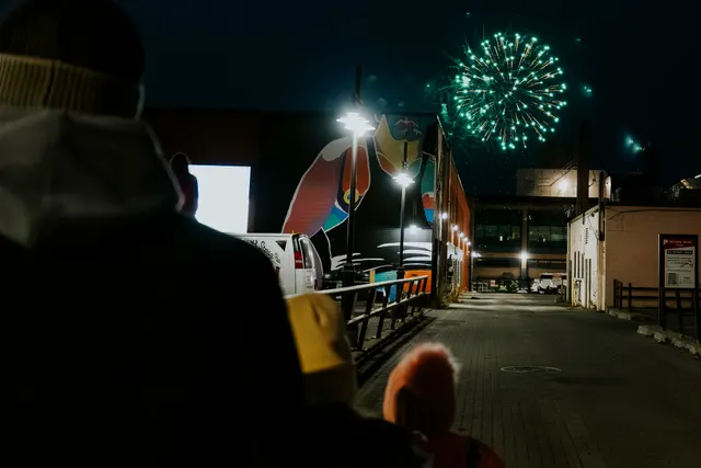 A green firework bursts over downtown Sudbury as spectators watch from the street below.
