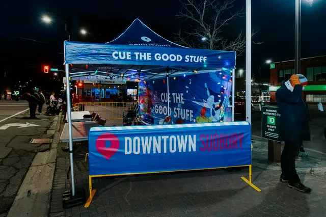 A Downtown Sudbury tent on the parade route, branded 'Cue the Good Stuff'.
