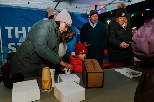 A parent and child collect hot chocolate at a table under a tent on the route.