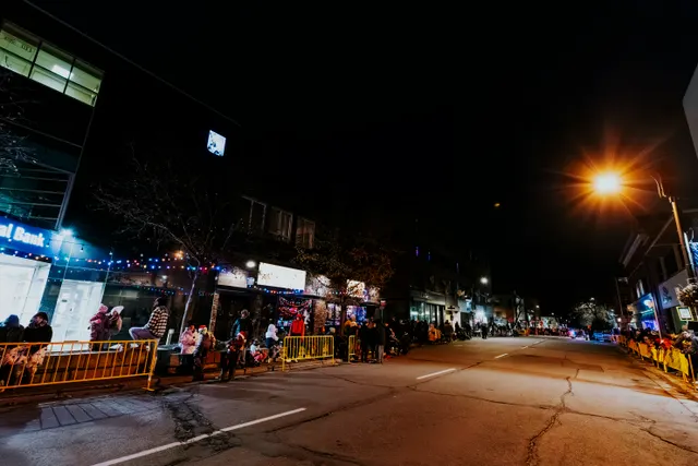 Spectators line both sides of an empty street lit by streetlamps and storefronts at night.