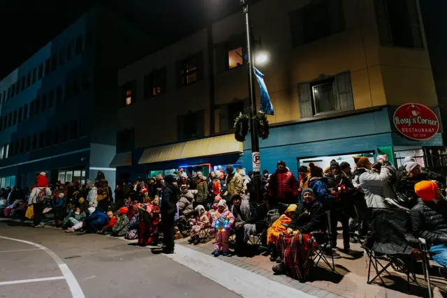 Spectators bundled in blankets and lawn chairs wait outside Rosy’s Corner Restaurant at night.
