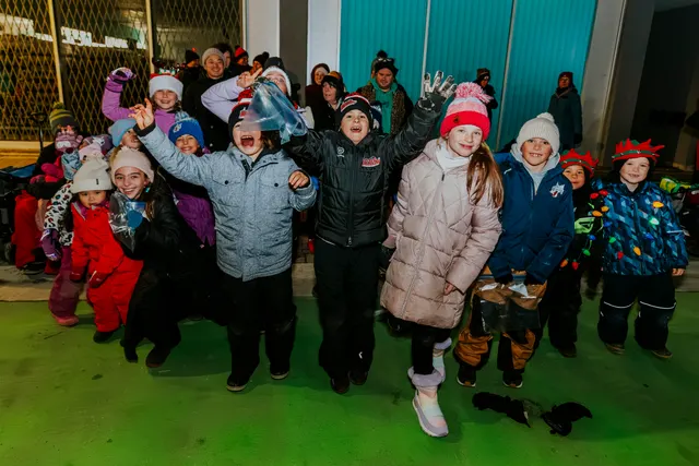 A group of children in winter coats cheer with their arms raised as the parade passes.
