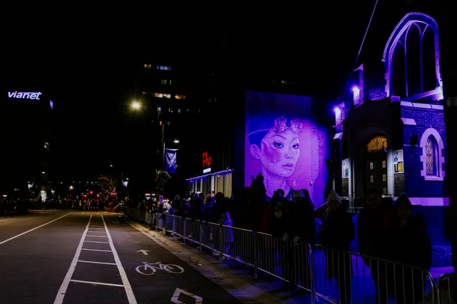 A downtown mural lit in purple as spectators line the barricades in front of it.