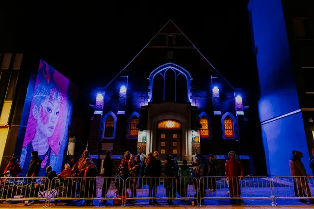 The Church of the Epiphany lit in blue and purple with people gathered outside.