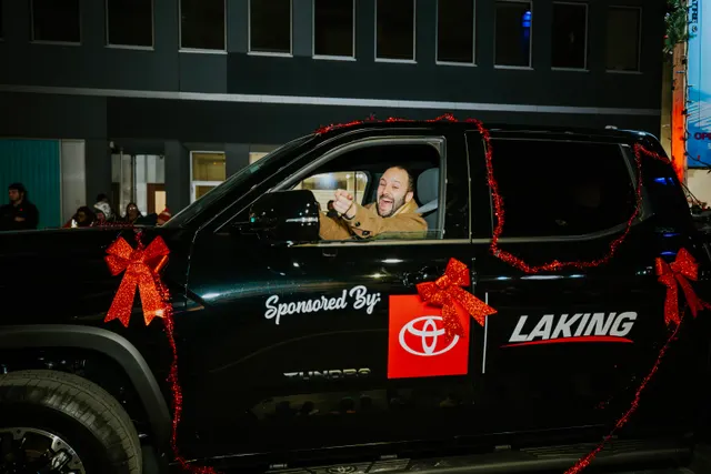 A driver waves from a black pickup truck decorated with red bows, marked Sponsored By Laking.