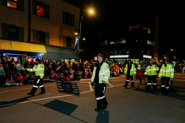 Marshals in high-visibility jackets walk the parade route carrying a Santa Claus Parade sign.