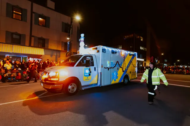 A decorated ambulance strung with lights, topped with a snowman figure, drives the parade route.