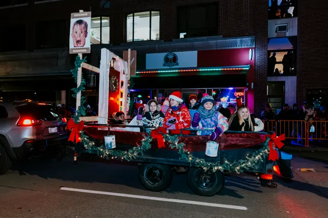 Children wave from a small trailer float decorated with garland, lights and red bows.