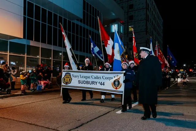 Cadets in Santa hats carry flags and a banner reading Navy League Cadet Corps Sudbury 44.
