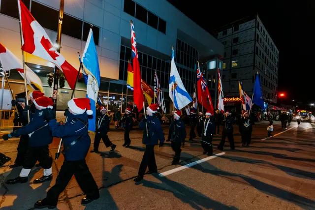 Uniformed cadets in Santa hats march carrying Canadian and organizational flags at night.