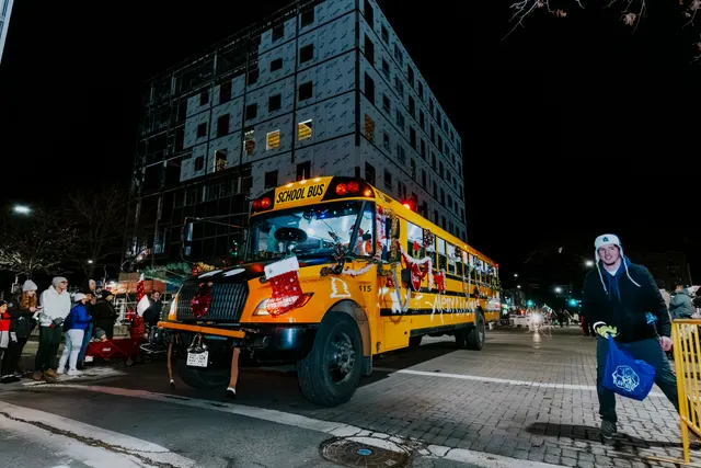 A yellow school bus decorated with lights and characters drives the parade route at night.