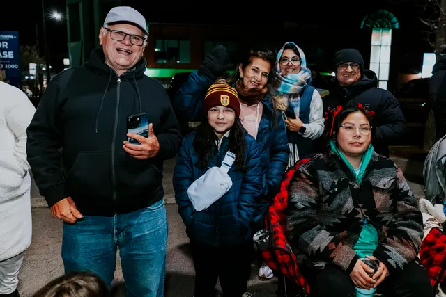 A family bundled in winter coats smiles for a photo at the parade at night.
