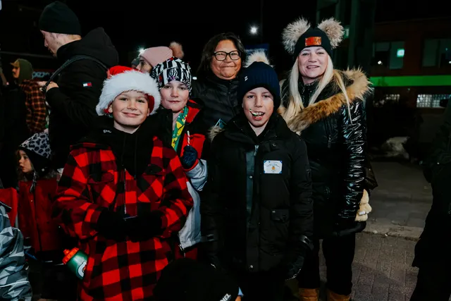 A group of children and an adult pose together smiling at the parade at night.