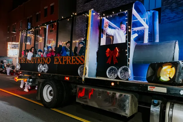Riders wave from the Neutrino Express float as it passes the crowd.