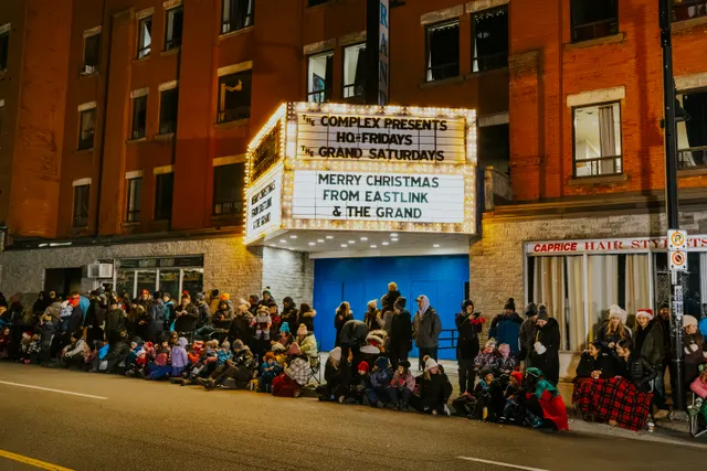 The Grand's marquee reads 'Merry Christmas from Eastlink and The Grand' above a crowd seated along the curb.