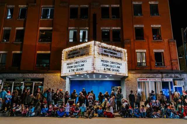 A crowd of families sits beneath a theatre marquee reading Merry Christmas from Eastlink and The Grand.