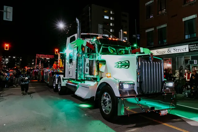 A transport truck lit end to end in green drives the parade route at night.