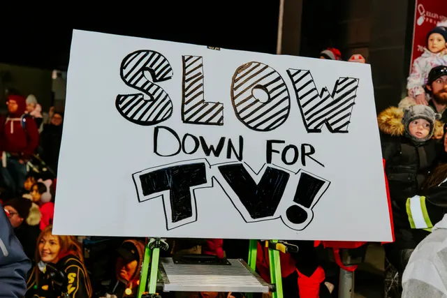 A spectator holds up a handmade sign reading Slow Down For TV amid the crowd.