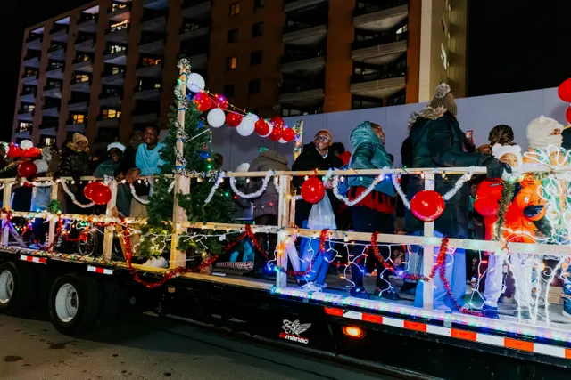 Riders wave from a flatbed float trimmed with garland, balloons and a small Christmas tree.