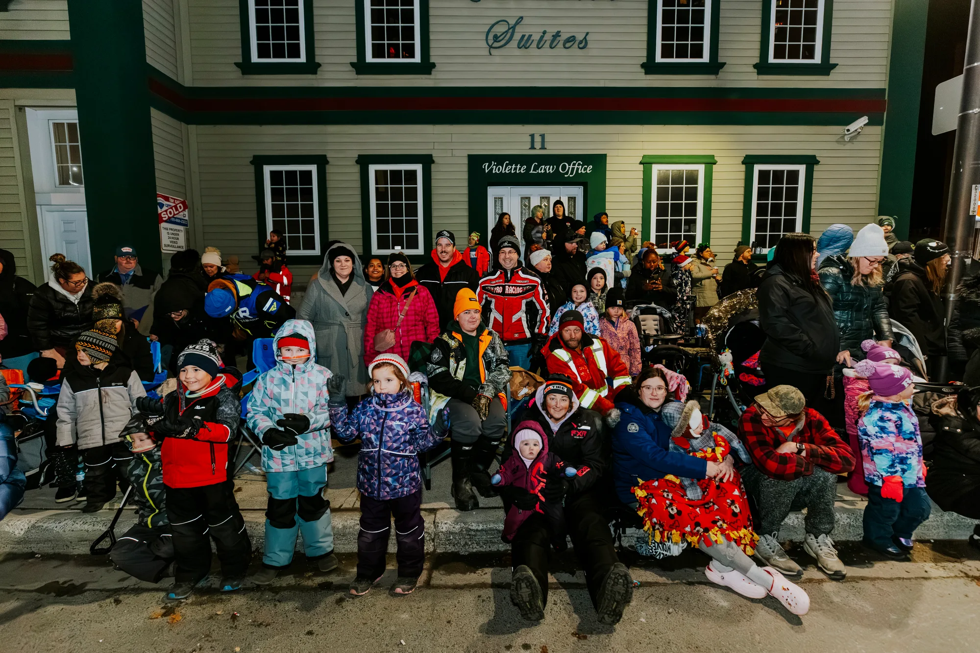 Children in winter coats watch the parade from behind a barricade, some waving.