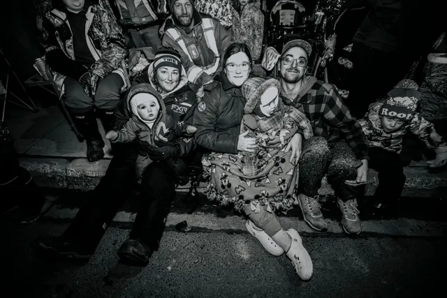 A family sits together on the curbside, a bundled toddler held close, in black and white.
