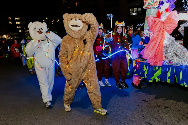 A performer in a bear costume strung with lights waves to the crowd.