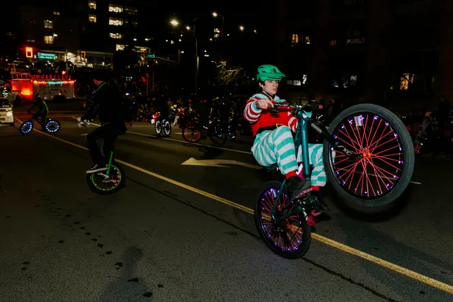 A rider pops a wheelie on a BMX bike with glowing spoke lights down the parade route.