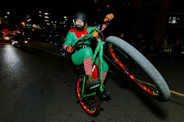 A rider dressed as an elf performs a wheelie on a bike with glowing spokes.