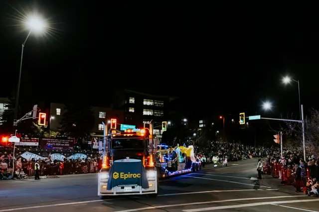 An Epiroc-branded truck tows a brightly lit float past crowds at a traffic signal.