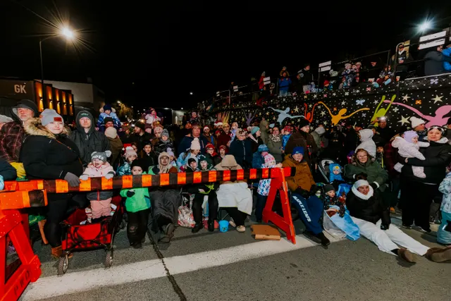 Families wait behind a striped barrier beneath a fence decorated with colorful star cutouts.