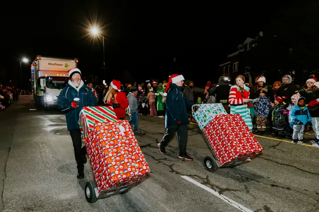 Two walkers pull giant wrapped-present carts down the parade route past a crowd.