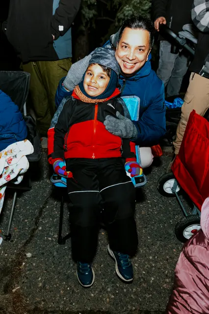 A child in a red and black coat is held up at the barricade to see over the crowd.