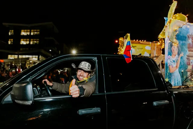 A driver gives a thumbs up from a truck flying a small Colombian flag, towing a decorated float.
