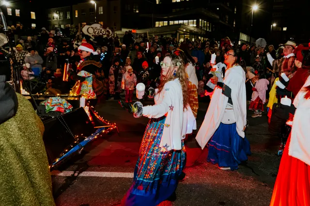 Costumed performers in colorful dresses carry lit candles down the parade route.