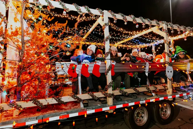A float hung with Christmas stockings and strings of warm lights carries riders in Santa hats.