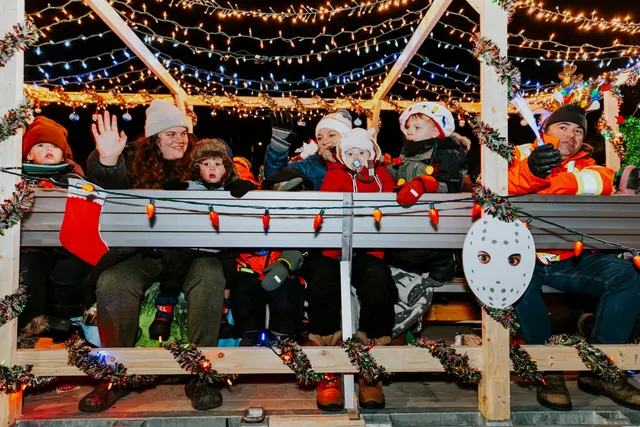Families ride a lit, garland-trimmed float, waving and smiling at the crowd.