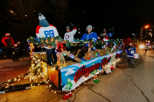 A float painted with 'Joyeux Noël' moves along the route, lit in warm white.